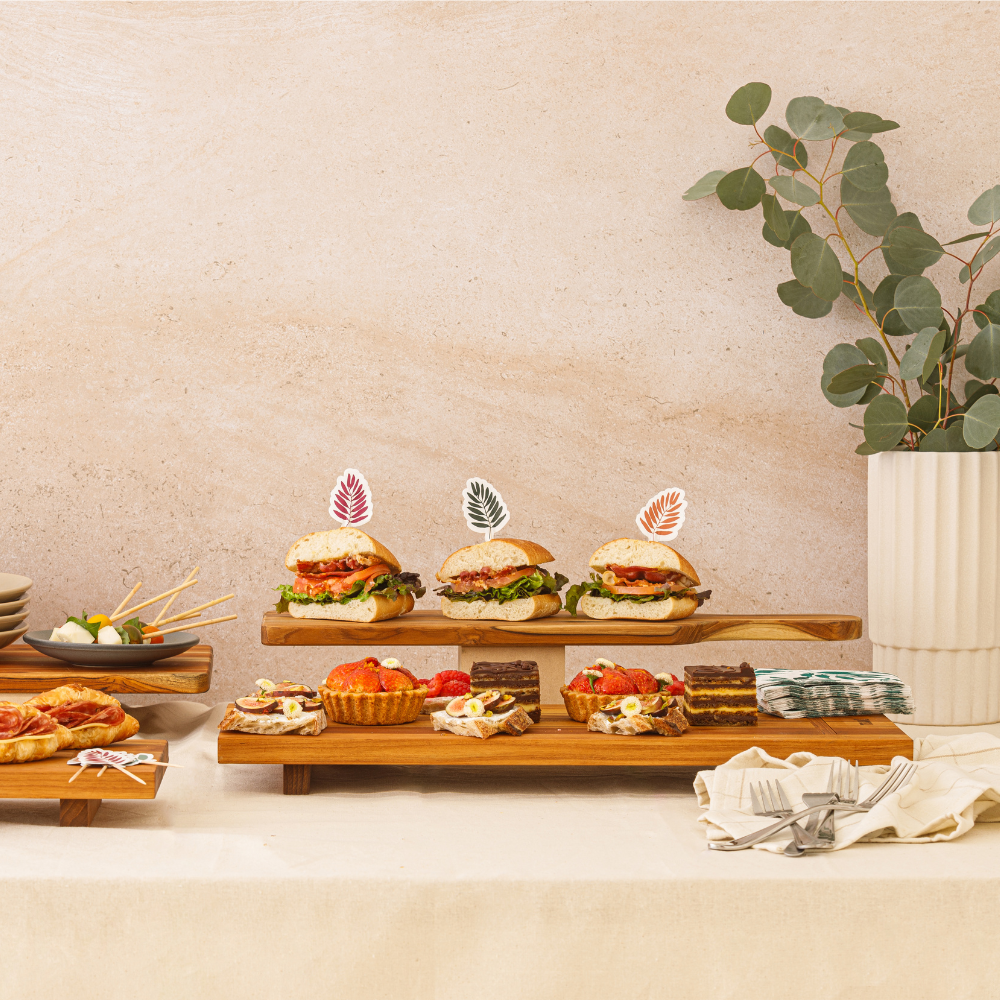 Modular teakwood food stand displaying mini sandwiches and gourmet pastries in an elegant tabletop setting.