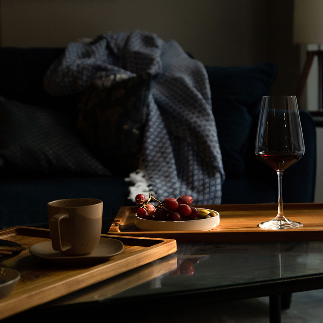 Nordic style teak serving trays styled with grapes and a wine glass on a coffee table.
