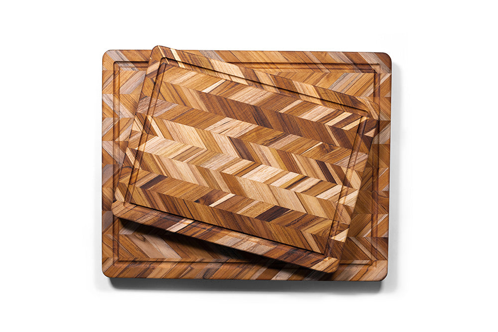 Stacked teak wood cutting boards featuring a rich herringbone pattern and integrated juice groove.