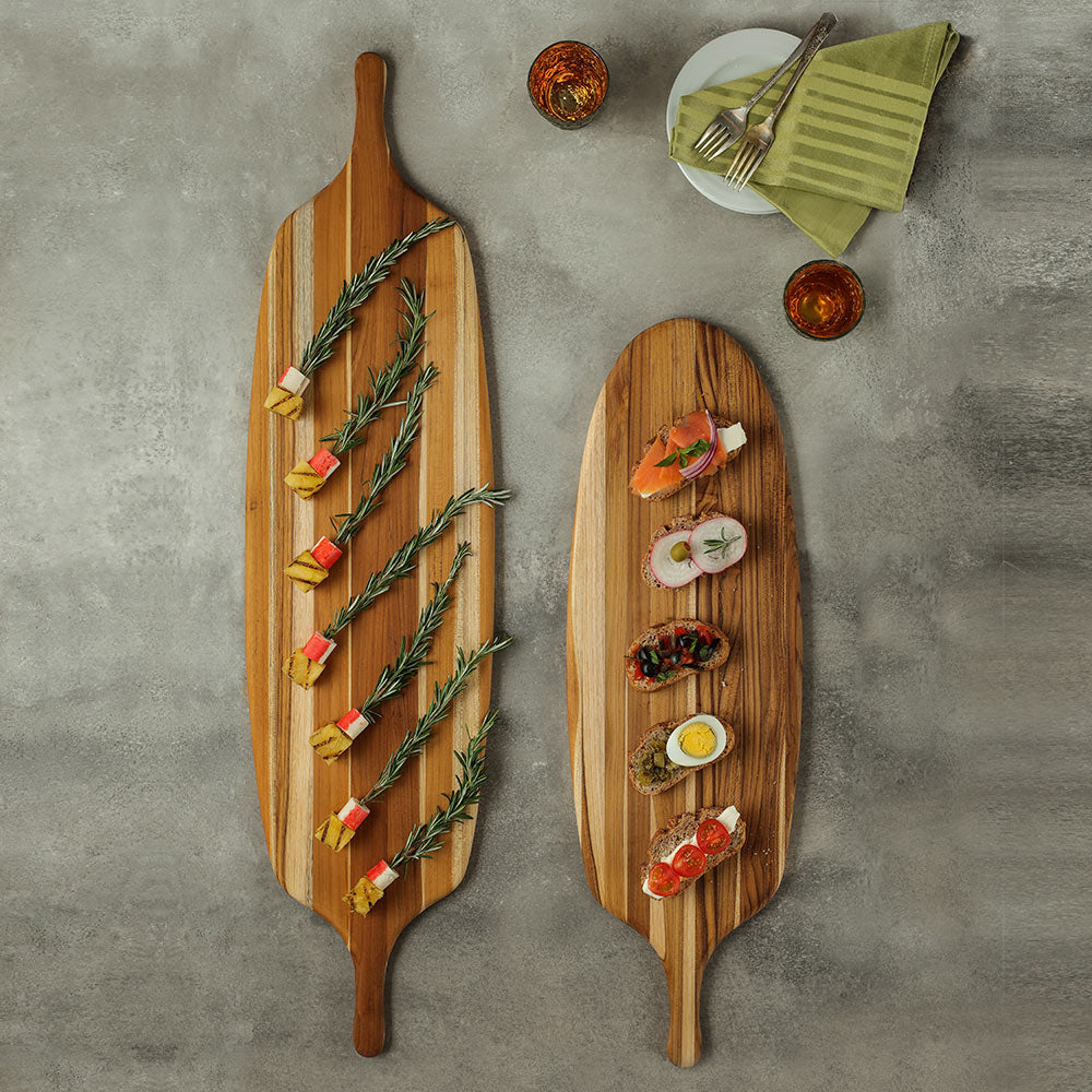 Teakwood paddle serving boards with appetizers on a gray textured background.