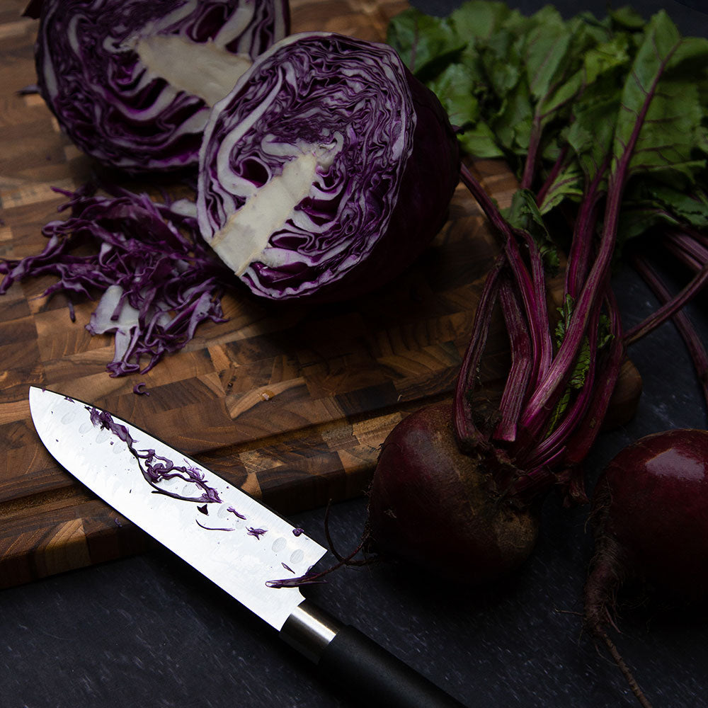 Teak end grain cutting board with juice canal, featuring fresh purple cabbage, beets, and a chef's knife.