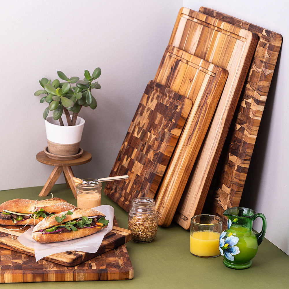 Stacked teakwood cutting boards in end grain and edge grain patterns displayed in a kitchen setting with food.