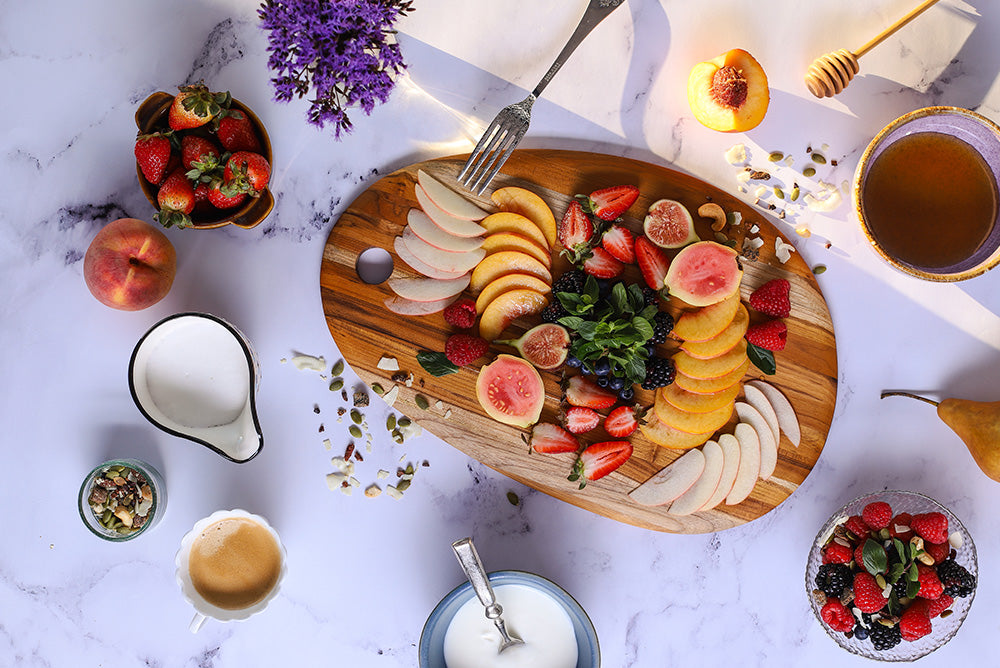 Elegant oval teak serving board topped with fresh fruit slices on a white marble background.