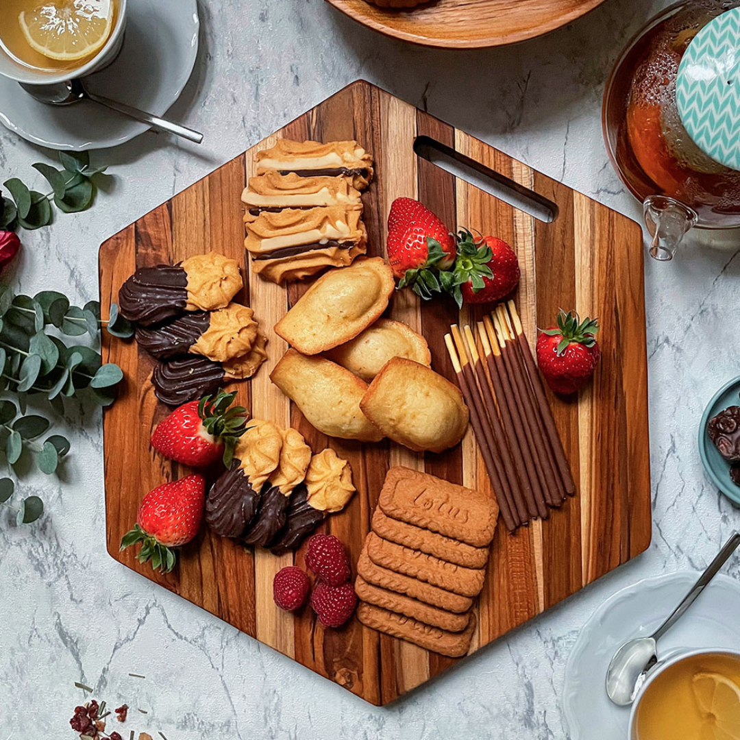 Hexagonal teakwood serving board styled with cookies, pastries, and fresh strawberries on a white marble table.