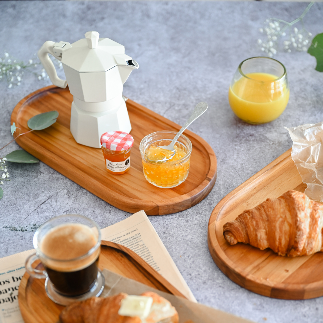 Essential oval teak wood serving tray styled with a white moka pot and jam jar on a grey surface.
