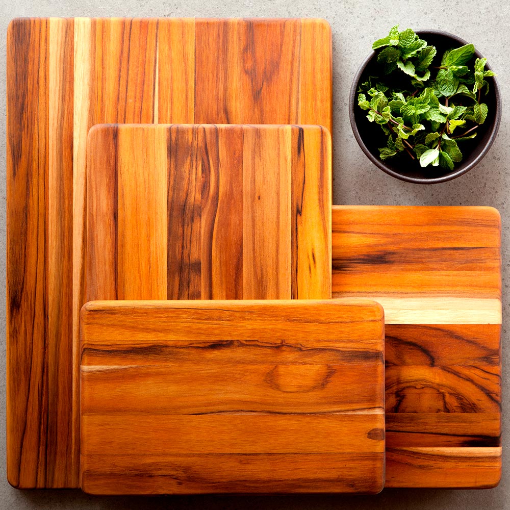 Stacked rectangular teakwood cutting boards with edge grain patterns next to a bowl of fresh mint leaves.