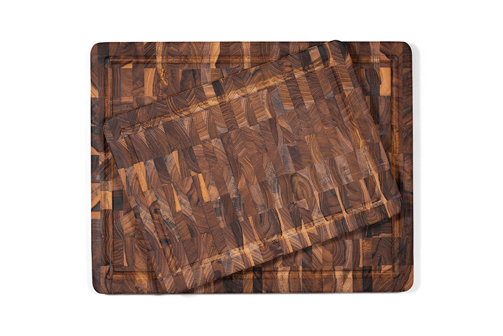 Stacked rectangular teak end grain cutting boards with juice canals and a natural checkerboard pattern.