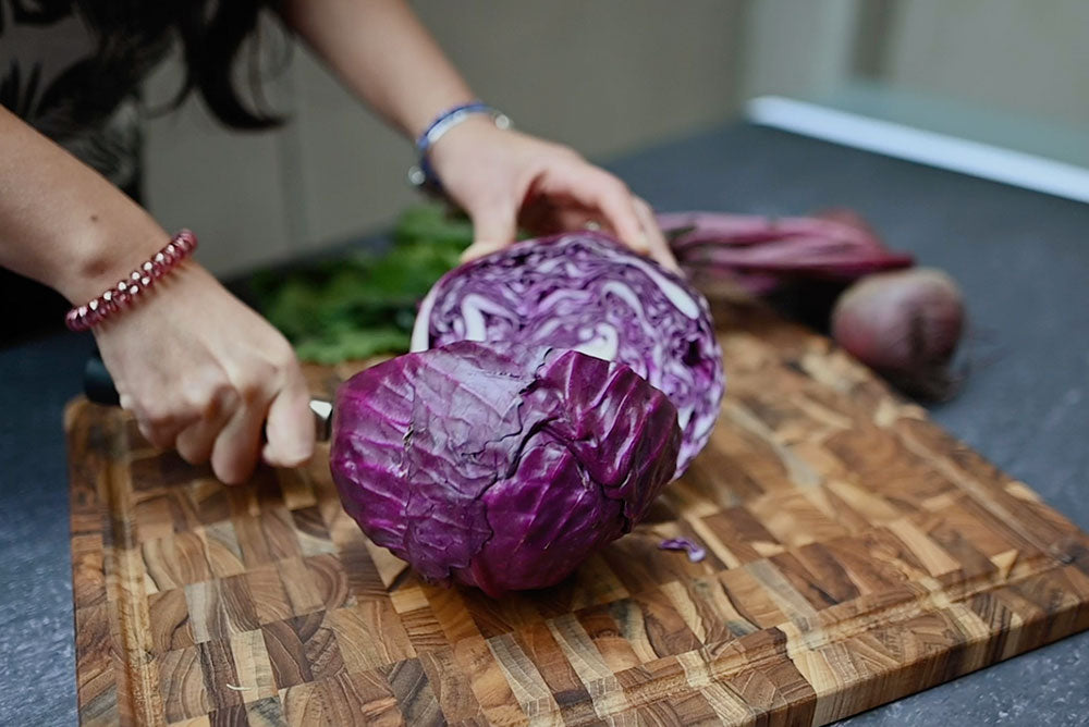 Teak end grain cutting board with a juice canal being used to slice a head of red cabbage.
